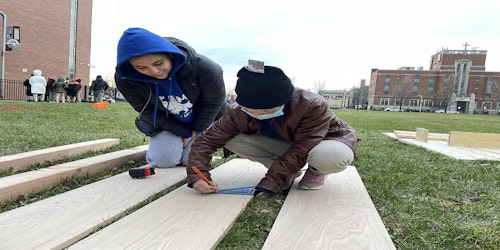 Two kids drawing on wood panel outdoors