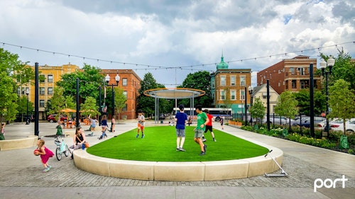 Children play on the raised lawn in Northcenter Town Square.